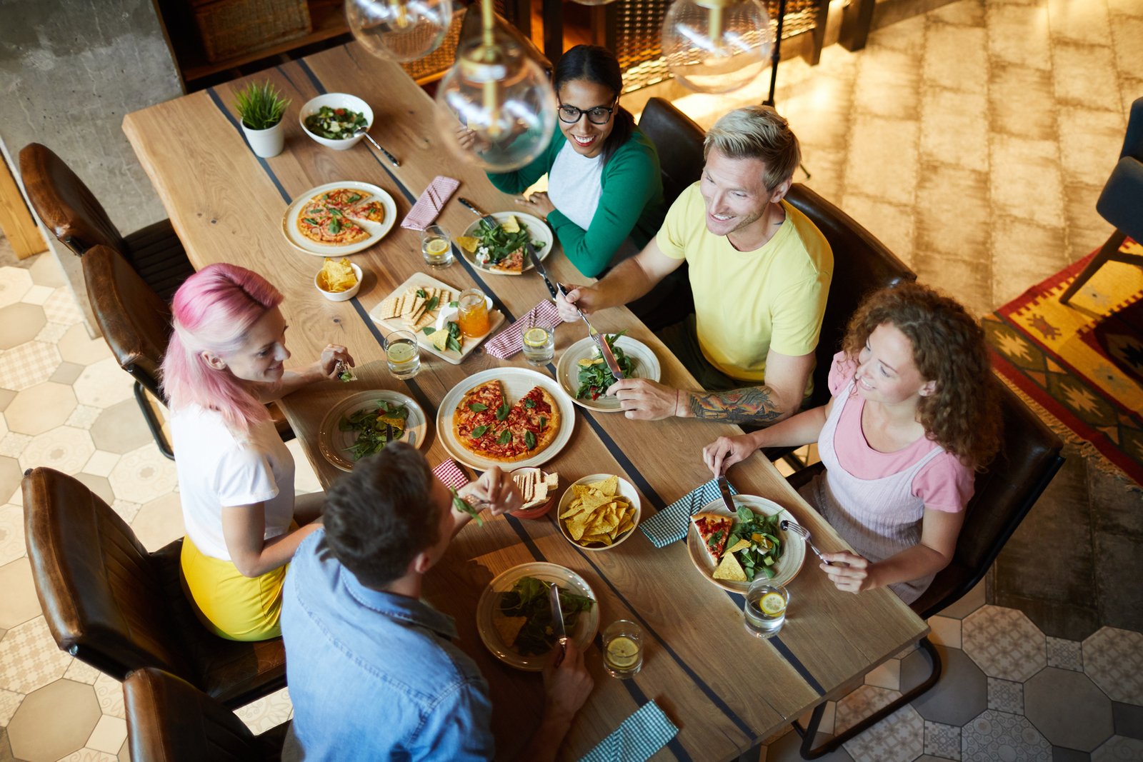 Overview of several young friends sitting by festive table in cafe and having talk
